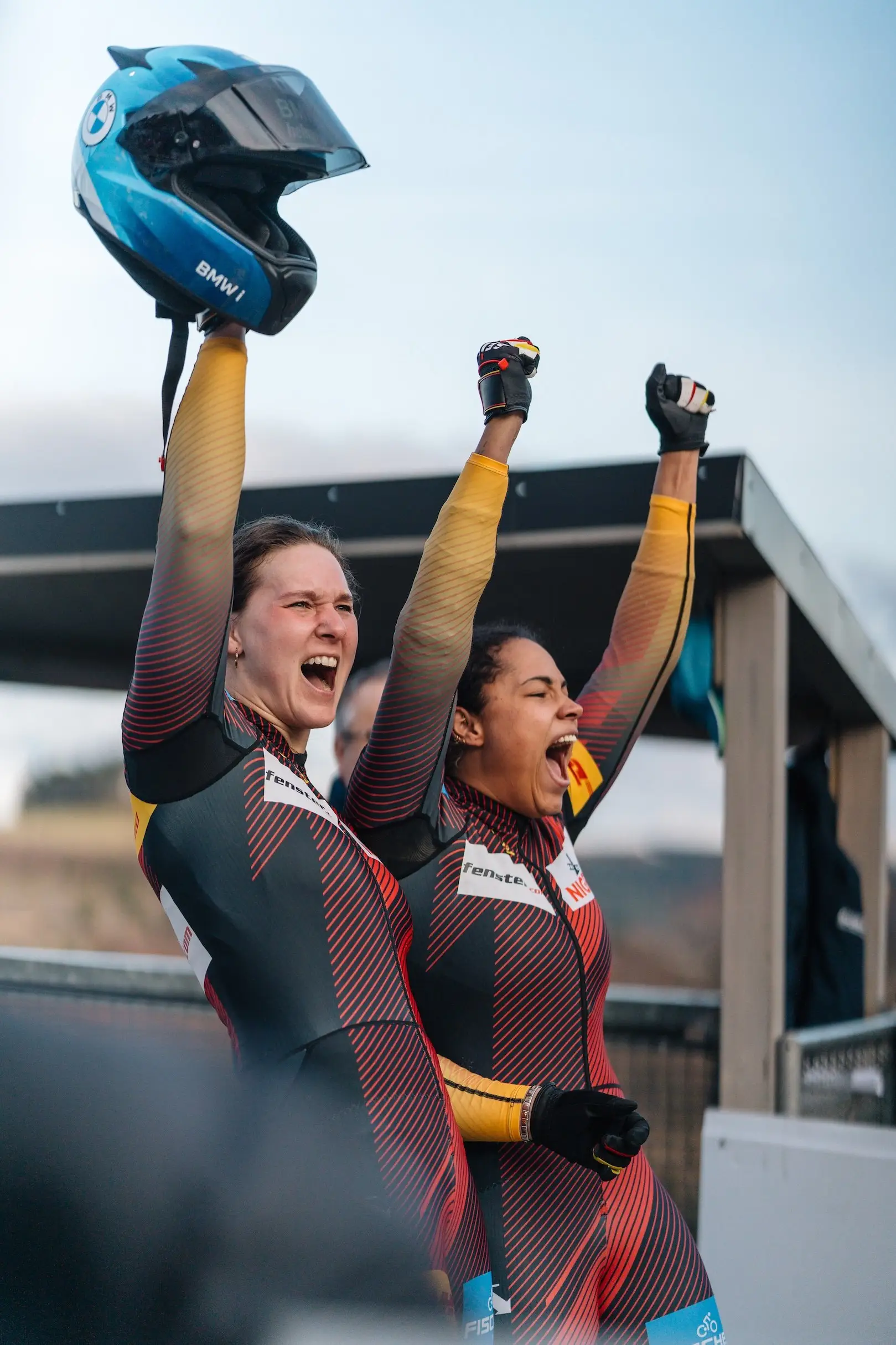 Two athletes cheering with raised arms, one holding a helmet