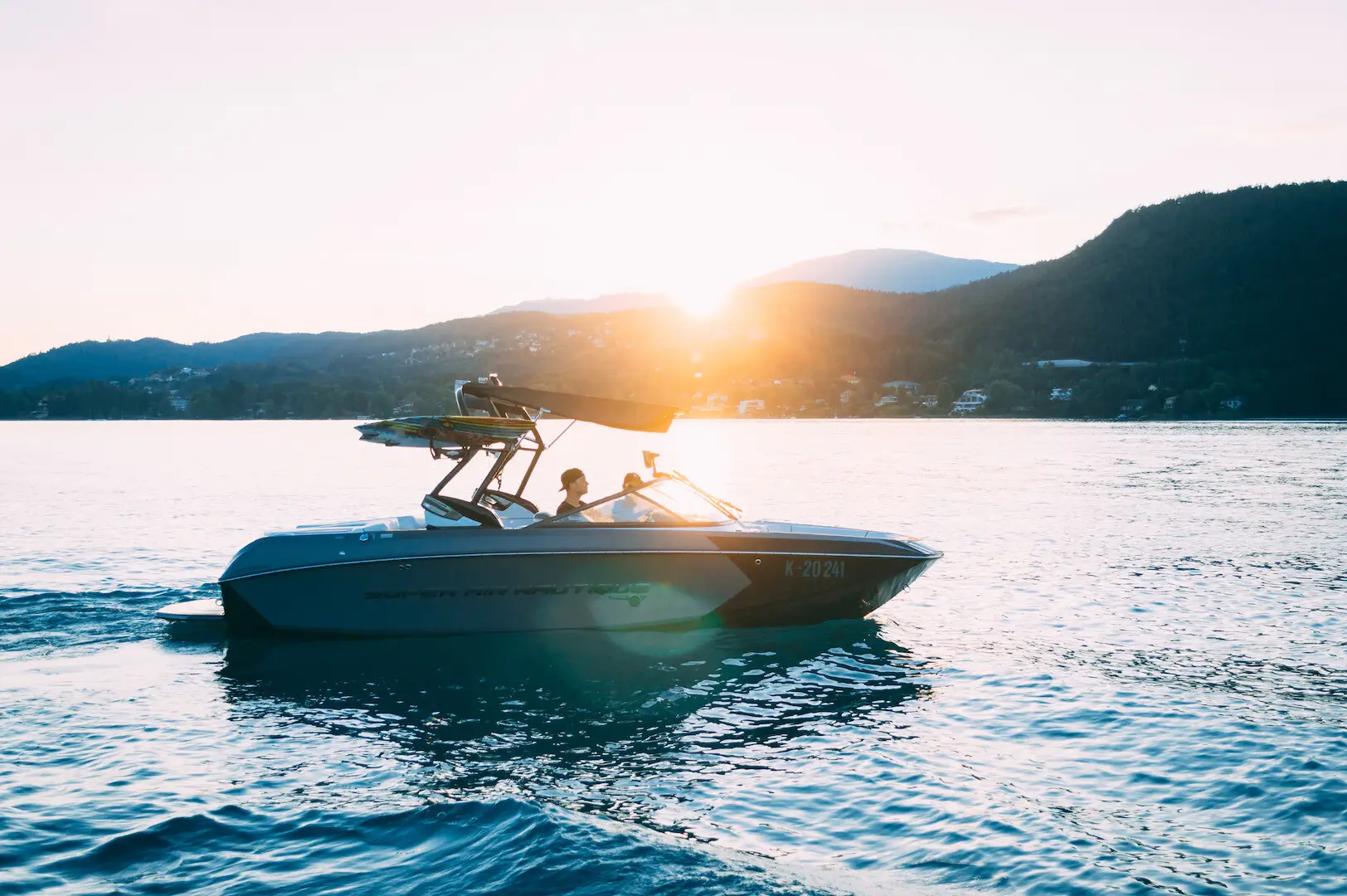 A Super Air Nautique wakesurf boat on Lake Wörthersee at sunset, hills behind