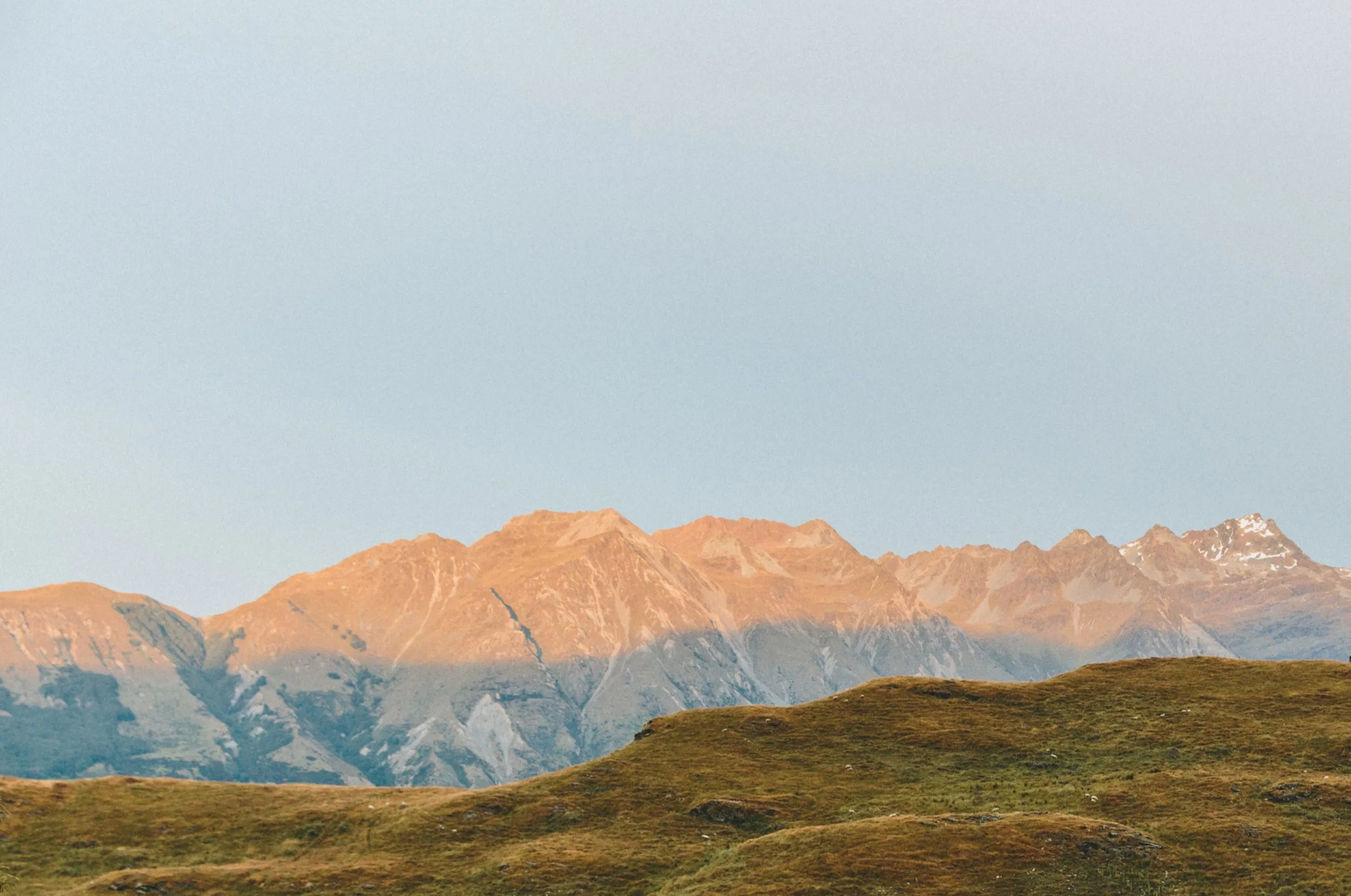 A mountain range catching the last sun above grassy hills